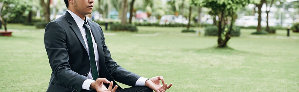 business person meditating in a field